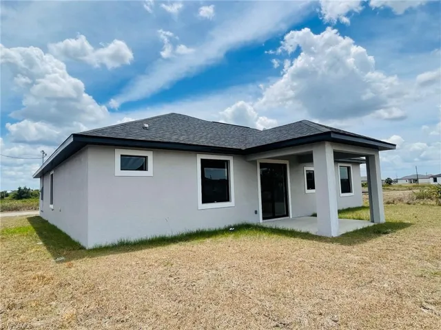 Rear view of house featuring a yard, a patio, roof with shingles, and stucco siding