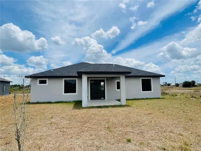 Rear view of property featuring a shingled roof, a patio area, stucco siding, and a yard