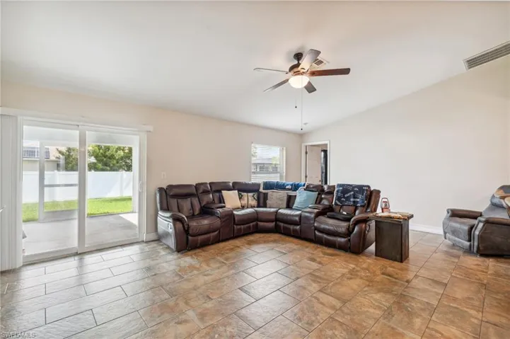 Living room featuring ceiling fan, light tile patterned flooring, and vaulted ceiling