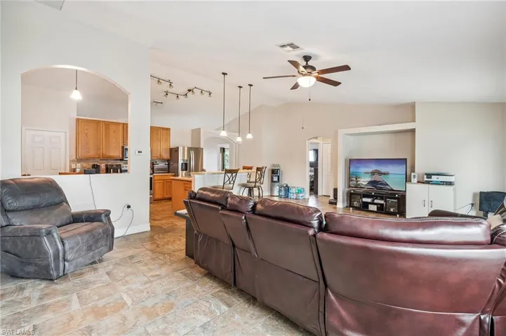 Living room featuring ceiling fan, light tile patterned floors, vaulted ceiling, and rail lighting
