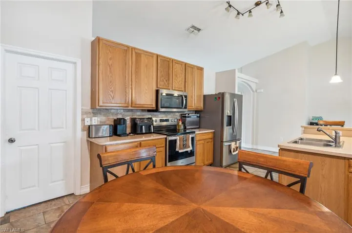 Kitchen featuring tasteful backsplash, stainless steel appliances, track lighting, light tile patterned floors, and sink