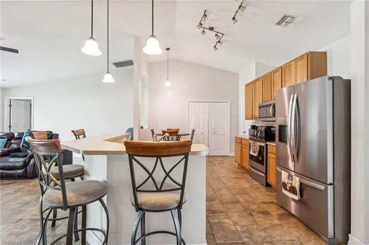 Kitchen with pendant lighting, tile patterned floors, stainless steel appliances, track lighting, and vaulted ceiling
