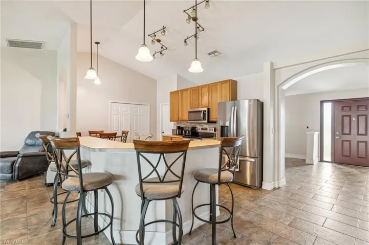 Kitchen featuring lofted ceiling, stainless steel appliances, a kitchen bar, and pendant lighting