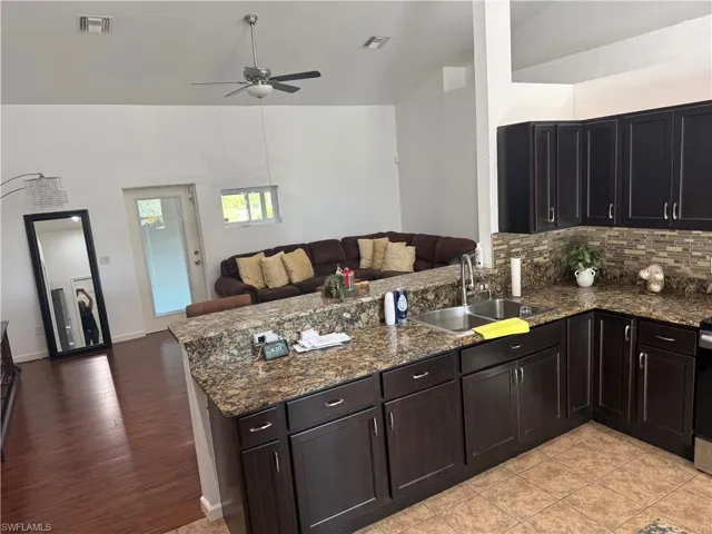Kitchen view from laundry room featuring open floor plan, dark stone counters, a peninsula, backsplash, and ceiling fan