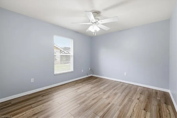 Room featuring wood-finish flooring, a ceiling fan with integrated lighting, and a single window with horizontal blinds