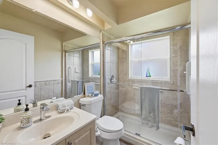Full bathroom featuring a single vanity with an integrated sink, a toilet, and a tiled shower with a glass enclosure