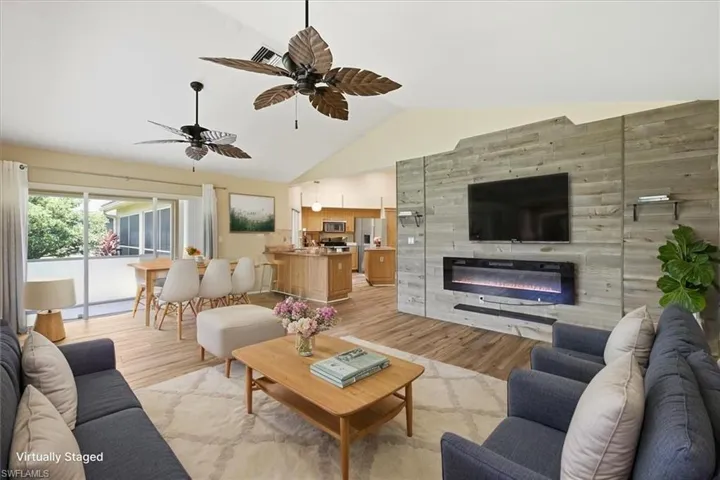 *VIRTUALLY STAGED* Spacious living area featuring vaulted ceilings, wood-finish flooring, a wall-mounted electric fireplace, and a kitchen with light wood cabinetry and a breakfast bar