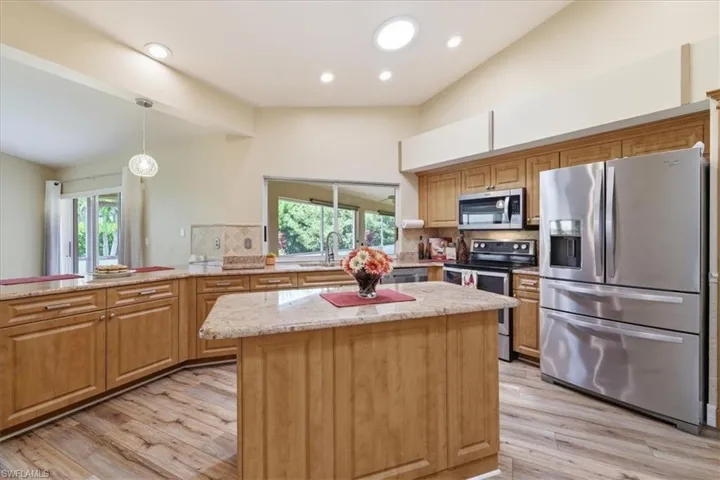 Kitchen featuring wood cabinetry, granite countertops, stainless steel appliances, a central island, and wood-finish flooring