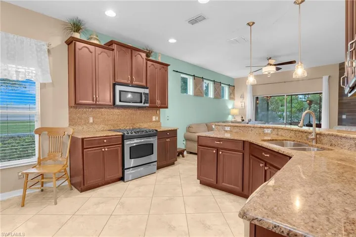 Kitchen with appliances with stainless steel finishes, hanging light fixtures, sink, decorative backsplash, and light tile patterned flooring