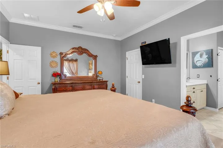 Bedroom featuring ensuite bath, ceiling fan, crown molding, and light tile patterned flooring