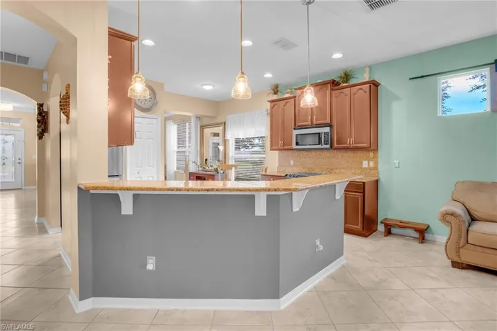Kitchen with a breakfast bar area, light tile patterned floors, decorative light fixtures, and tasteful backsplash