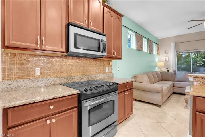 Kitchen featuring tasteful backsplash, stainless steel appliances, light stone countertops, ceiling fan, and light tile patterned flooring