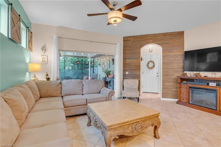 Living room with ceiling fan, light tile patterned floors, and wooden walls