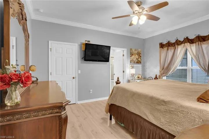 Bedroom with crown molding, light wood-type flooring, ensuite bath, and ceiling fan