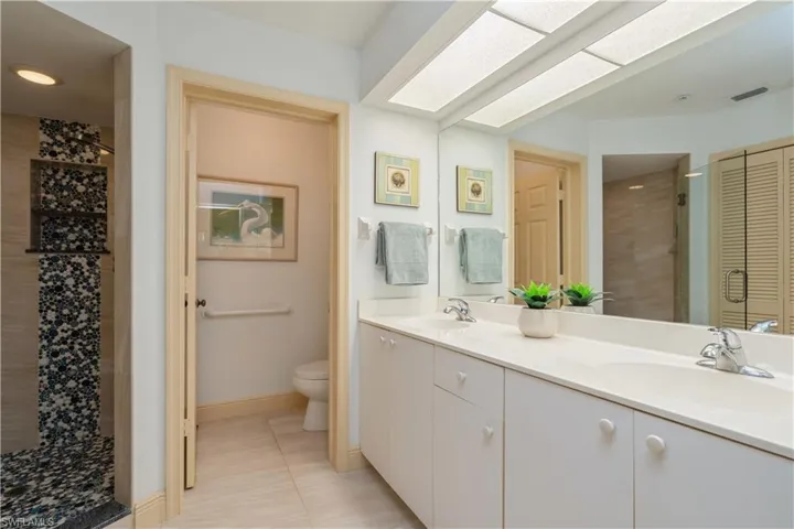 Bathroom featuring toilet, a skylight, tiled shower, vanity, and tile patterned flooring