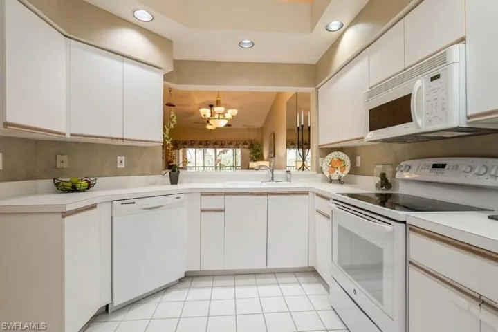 Kitchen featuring vaulted ceiling, a notable chandelier, light tile patterned floors, white cabinets, and white appliances