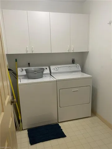 Laundry area with washing machine and clothes dryer, light tile patterned floors, and cabinets