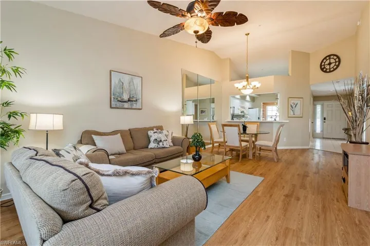 Living room with ceiling fan with notable chandelier, light wood-type flooring, and vaulted ceiling