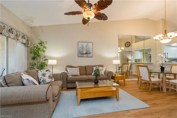 Living room featuring vaulted ceiling, ceiling fan with notable chandelier, and light wood-type flooring