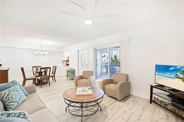 Living area featuring light wood-style flooring, a ceiling fan, a chandelier, and a textured ceiling