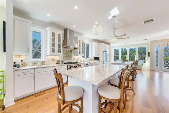 Kitchen with pendant lighting, wall chimney exhaust hood, a kitchen island, and white cabinetry