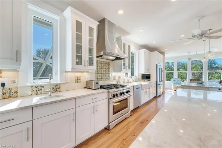 Kitchen featuring high end appliances, white cabinets, sink, light hardwood / wood-style flooring, and range hood