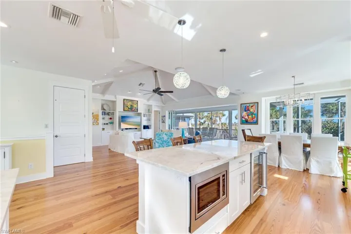 Kitchen featuring vaulted ceiling with beams, stainless steel microwave, white cabinetry, and a wealth of natural light