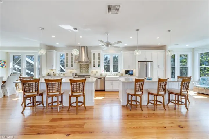 Kitchen with pendant lighting, stainless steel appliances, wall chimney range hood, and light wood-type flooring