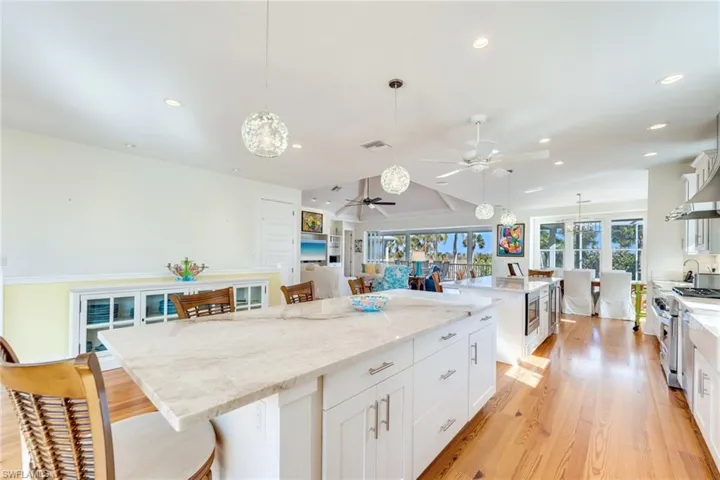 Kitchen with light wood-type flooring, a spacious island, decorative light fixtures, stainless steel stove, and white cabinetry