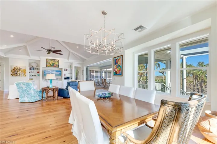 Dining area featuring lofted ceiling with beams, ceiling fan with notable chandelier, a wealth of natural light, and light hardwood / wood-style flooring