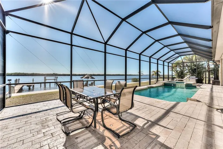 View of pool with glass enclosure, a water view, an in ground hot tub, and a patio