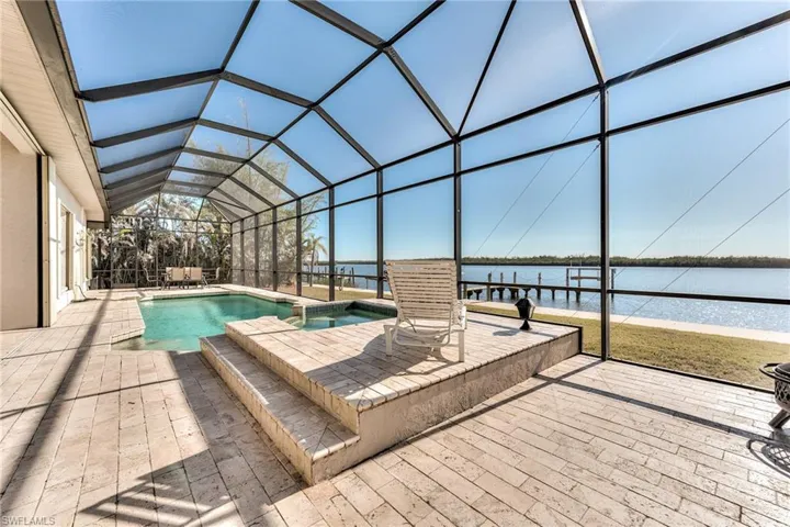 View of pool featuring glass enclosure, a water view, and a patio