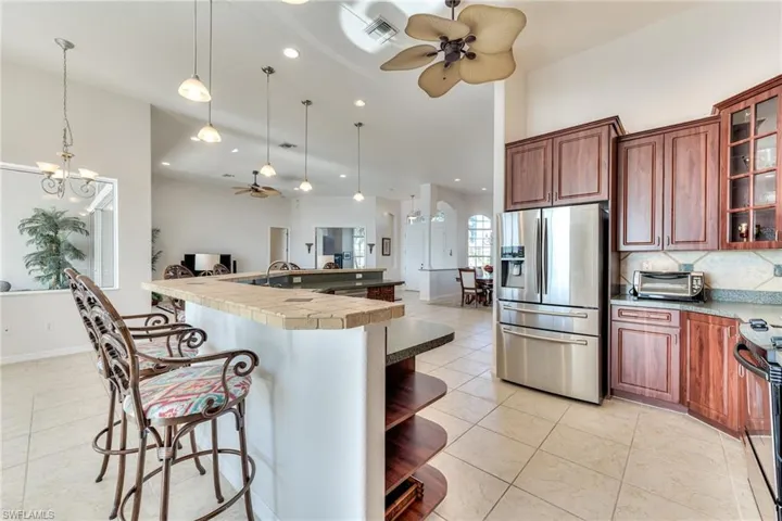 Kitchen featuring a kitchen breakfast bar, pendant lighting, stainless steel appliances, and ceiling fan with notable chandelier