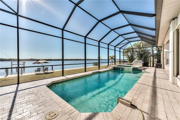 View of pool with glass enclosure, an in ground hot tub, a patio area, and a water view