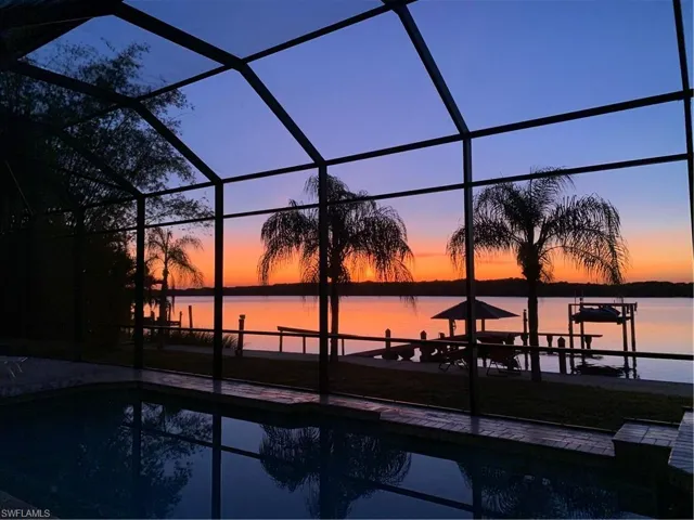 Pool at dusk featuring glass enclosure and a water view