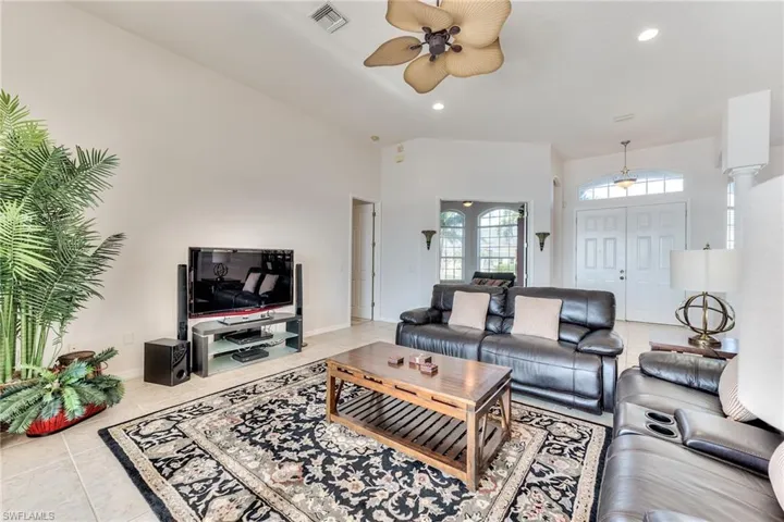 Tiled living room with a towering ceiling, decorative columns, and ceiling fan