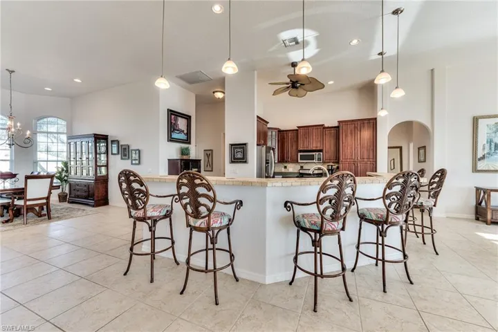 Kitchen with a breakfast bar, ceiling fan with notable chandelier, stainless steel appliances, pendant lighting, and light tile patterned floors