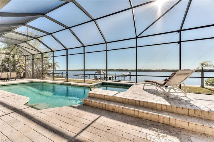 View of pool with an in ground hot tub, a patio, a water view, and glass enclosure