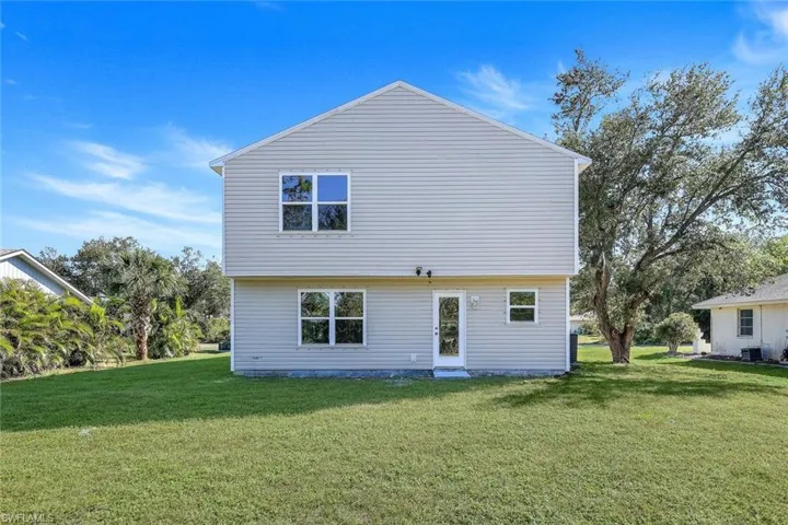 Back of property with central AC unit and a lawn