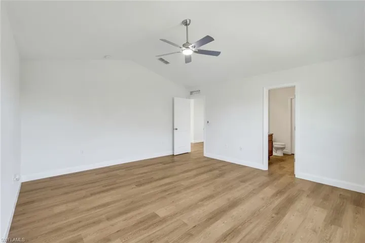 Unfurnished bedroom featuring ensuite bathroom, ceiling fan, light wood-type flooring, and vaulted ceiling