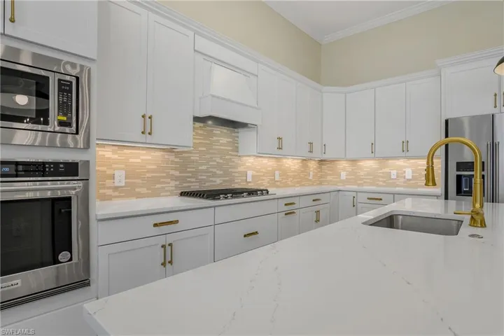 Kitchen featuring white cabinets, appliances with stainless steel finishes, premium range hood, and light stone countertops