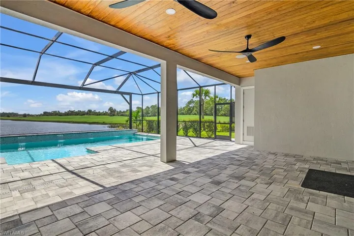 View of swimming pool featuring a patio area, pool water feature, glass enclosure, ceiling fan, and a water view