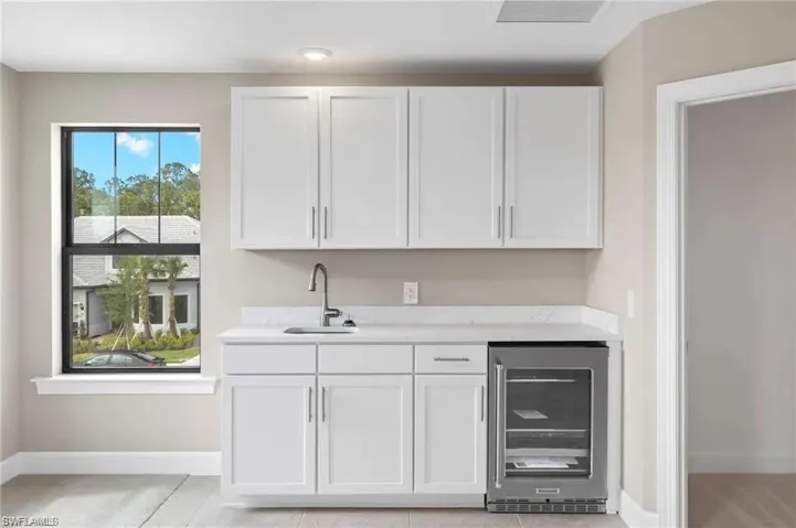 Bar with light stone counters, wine cooler, sink, and white cabinets