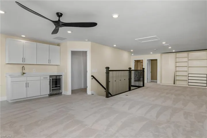 Unfurnished living room featuring ceiling fan, wine cooler, light carpet, and wet bar