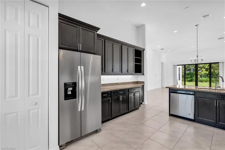 Kitchen with light tile patterned flooring, sink, appliances with stainless steel finishes, light stone counters, and pendant lighting