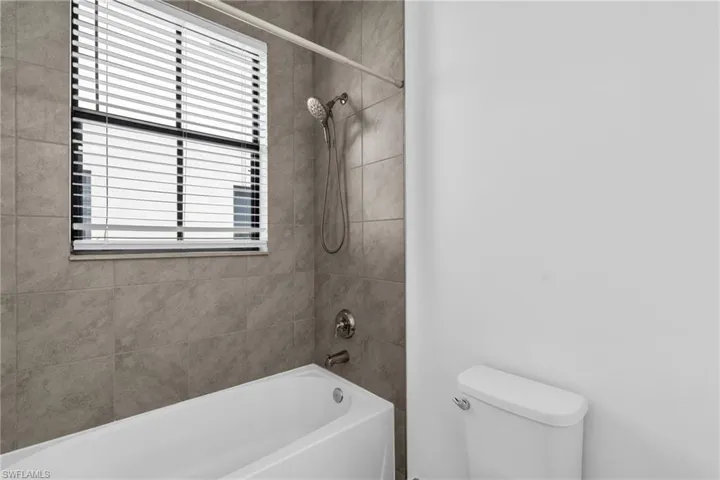 Bathroom featuring a wealth of natural light, tiled shower / bath combo, and toilet