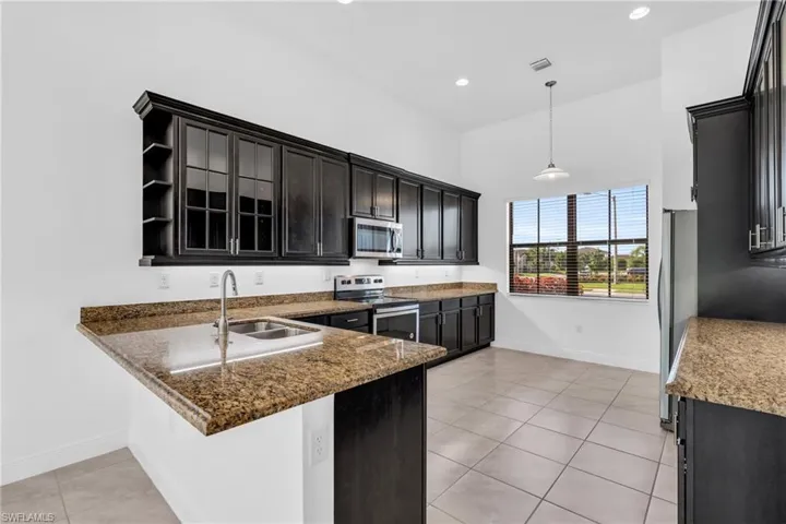 Kitchen with sink, dark stone countertops, appliances with stainless steel finishes, light tile patterned floors, and kitchen peninsula