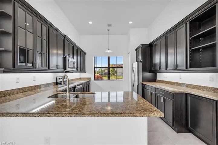 Kitchen with dark stone counters, light tile patterned flooring, sink, decorative light fixtures, and dark brown cabinetry