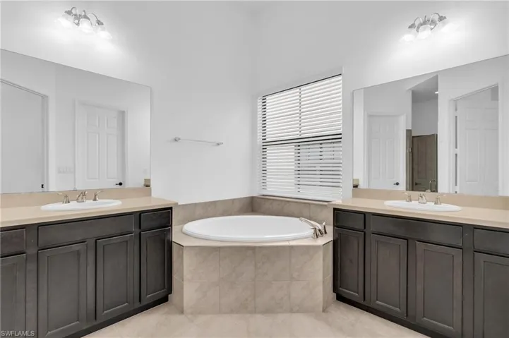 Bathroom featuring a relaxing tiled tub, double sink vanity, and tile patterned floors