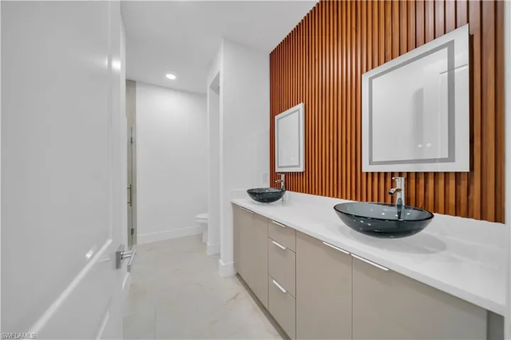 Bathroom featuring double vanity, recessed lighting, light marble finish floors, a stall shower, and an accent wall